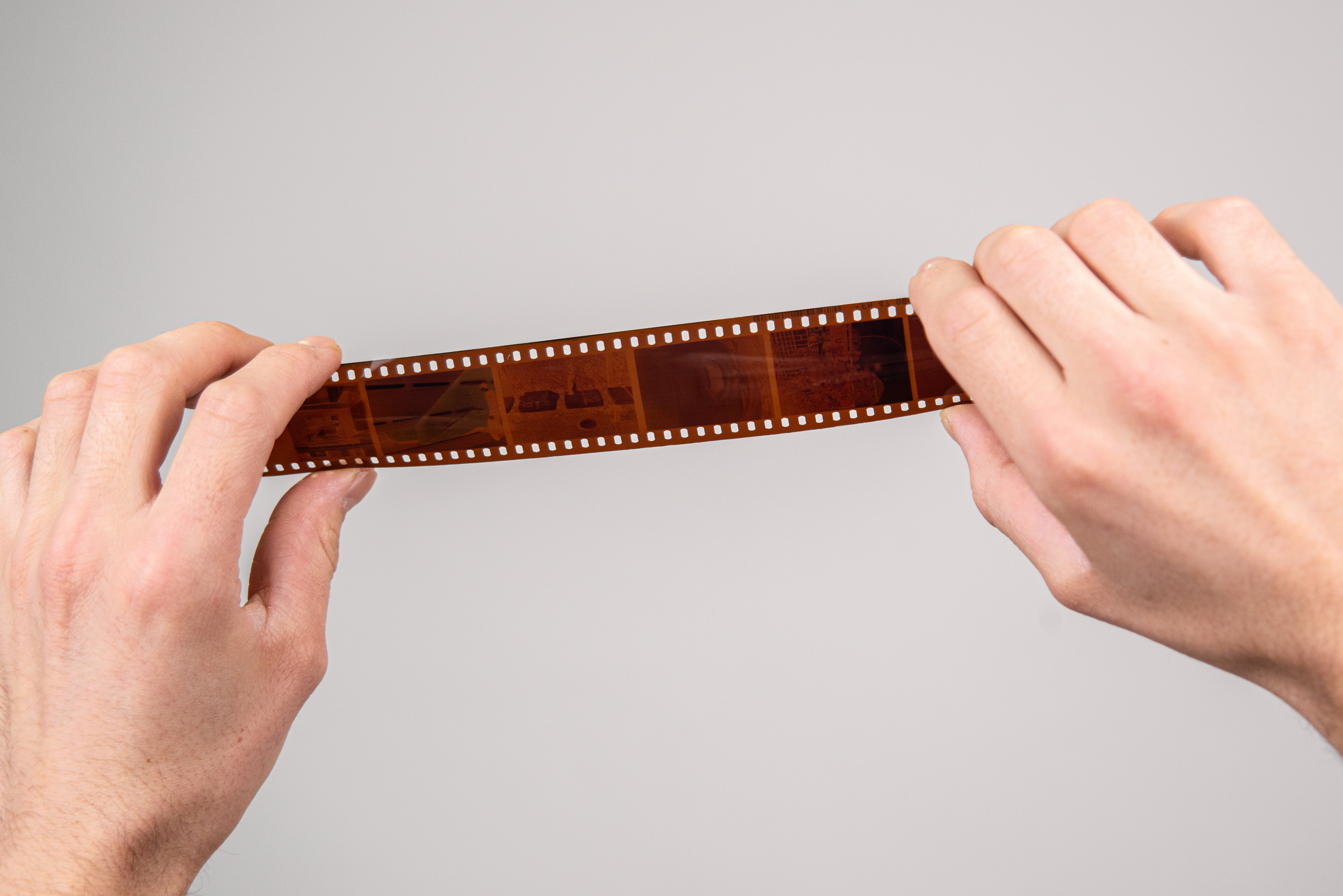 Film strip held between two hands against a gray background